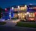 Modern suburban home illuminated with red, white, and blue LED flood lights, wall washers, strip lights, and pathway lighting for a 4th of July outdoor celebration at night.